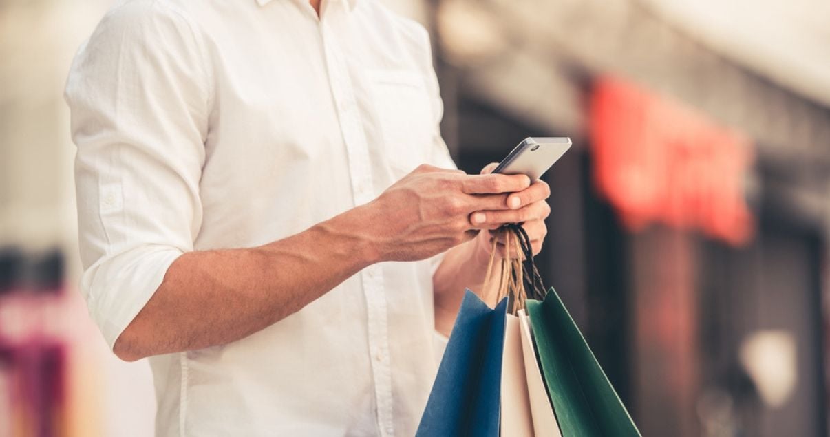 hombre de camisa amarilla sosteniendo bolsas y comprando en ecommerce en su celular