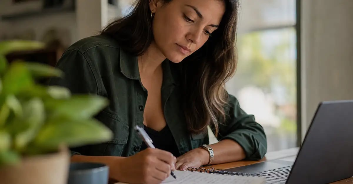 Profesional latinoamericana revisando una lista de verificación escrita a mano junto a una laptop