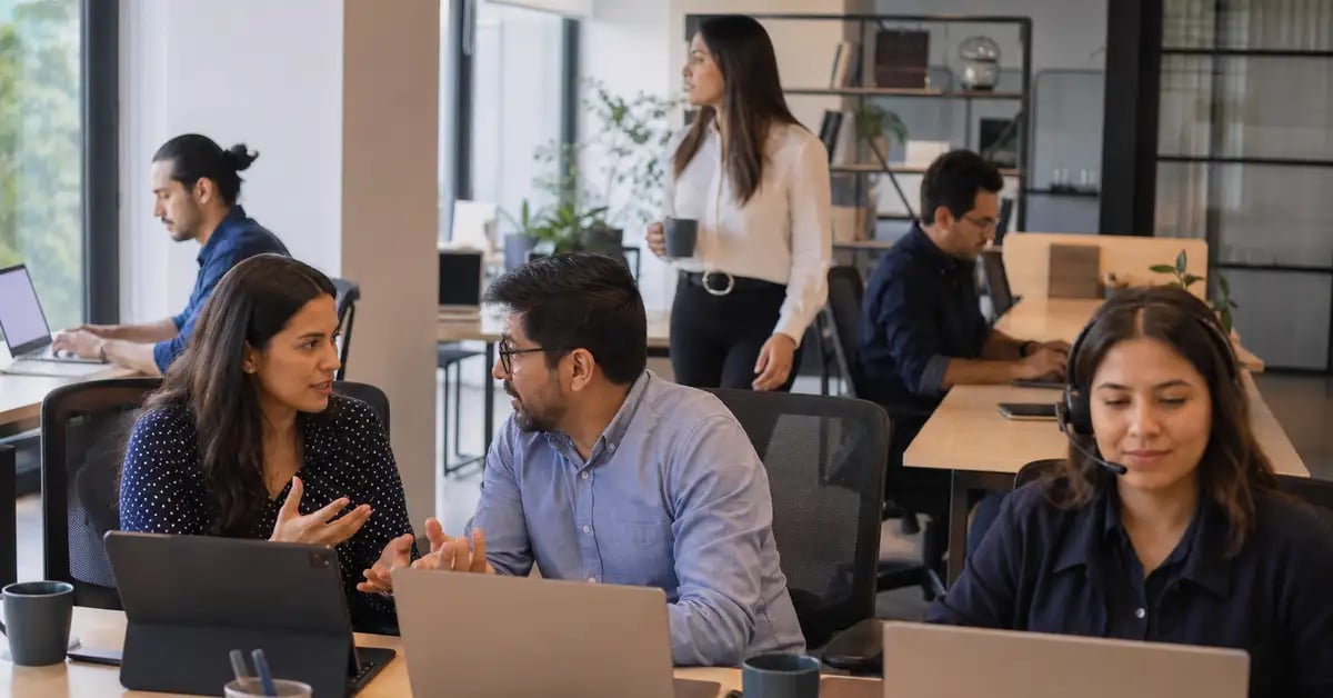Equipo latinoamericano en una oficina abierta con personas trabajando de formas distintas: en pareja, en llamada y de forma individual