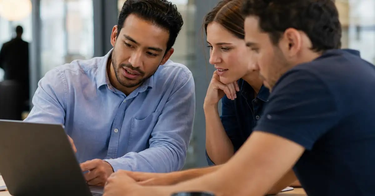 Consultor latinoamericano acompañando a dos personas del equipo cliente frente a una laptop durante una sesión de incorporación