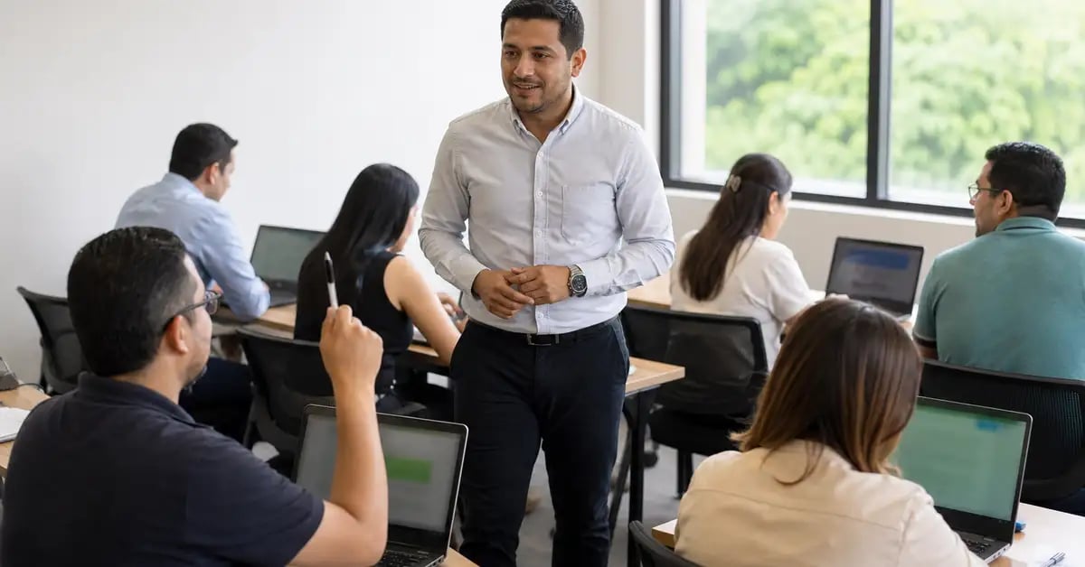 Formador latinoamericano acompañando a seis colegas que trabajan en sus laptops durante una sesión de habilitación