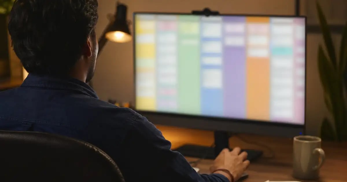 Vista sobre el hombro de una persona trabajando frente a un monitor con columnas de colores que representan un tablero de negocios