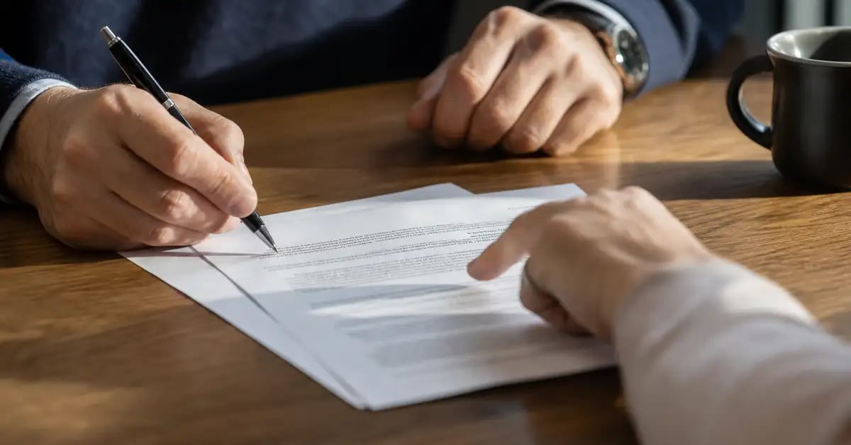 Manos revisando un contrato impreso sobre un escritorio, con bolígrafo y páginas apiladas